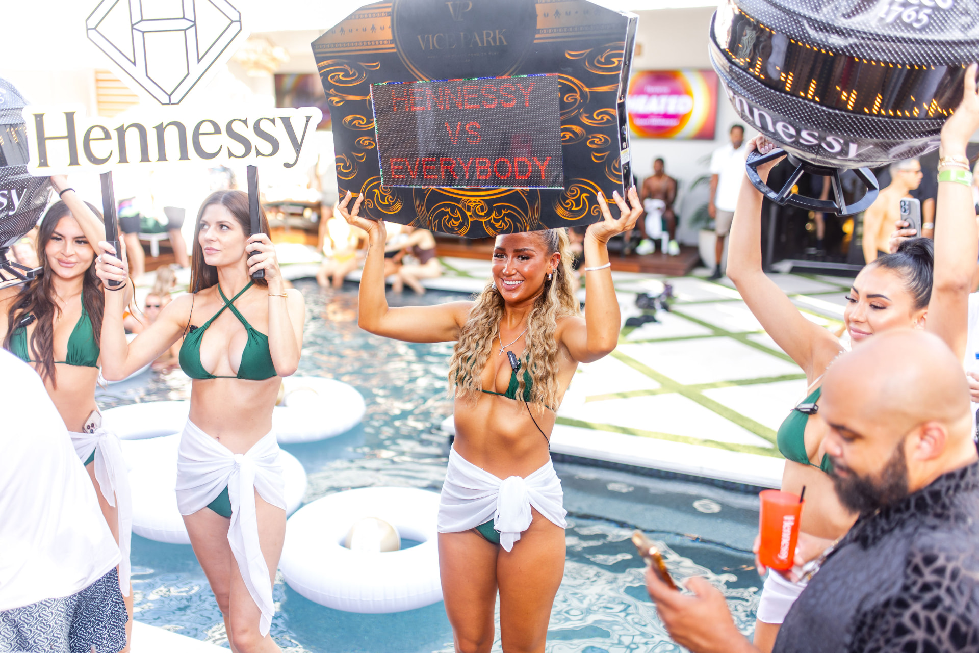 Crowded pool at Vice Park with staff holding Hennessy vs Everybody LED signage and branded signs