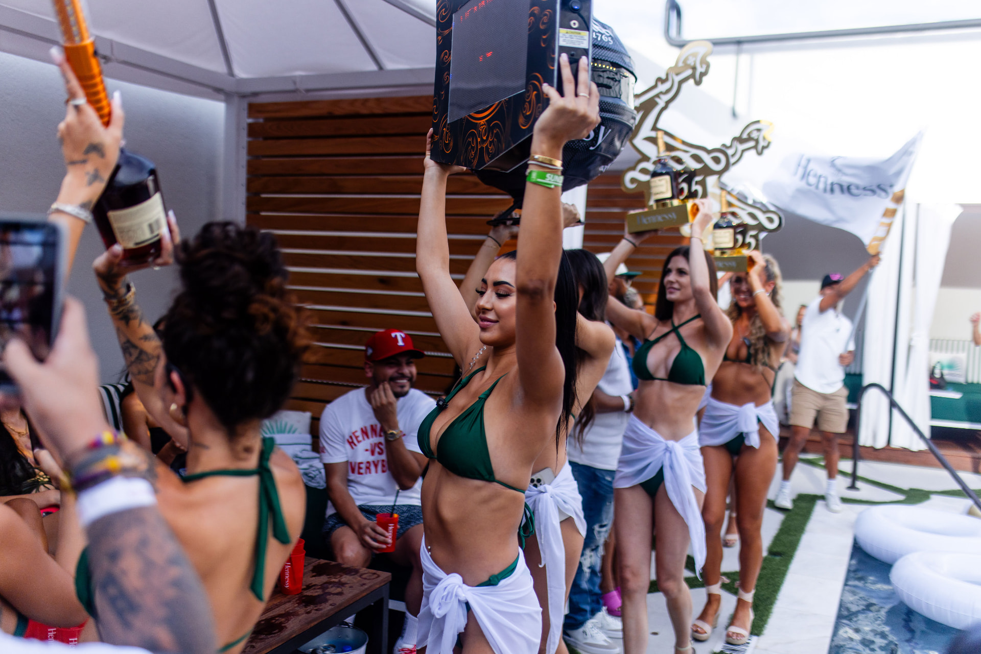 Hostesses carrying Hennessy bottles and trophies to a poolside cabana at Vice Park