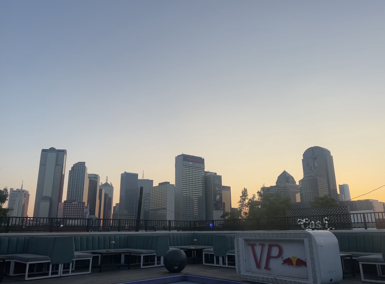 Golden-hour Dallas skyline viewed from the Vice Park rooftop, with the VP sign and greek-key railing in the foreground