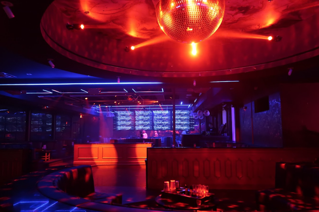 Vice Park main room with a disco ball, red-and-blue lighting, curved booths, and the illuminated bar wall