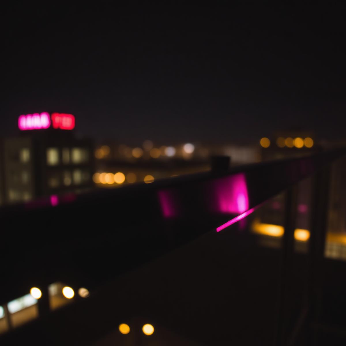 Magenta neon glow across the rooftop railing at night